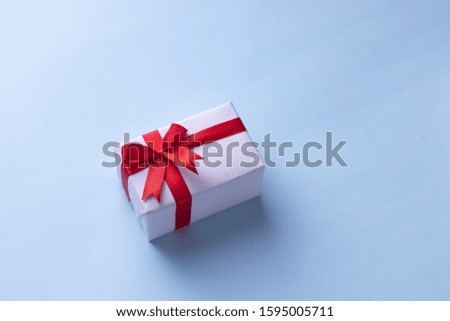 White gift box with red ribbon, light blue background flat lay for stock image.  