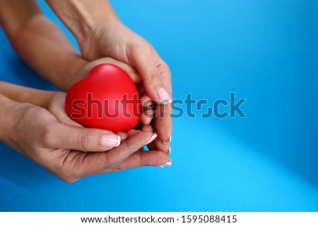 Mother and daughter hold red heart against blue background closeup. Happy childhood concept