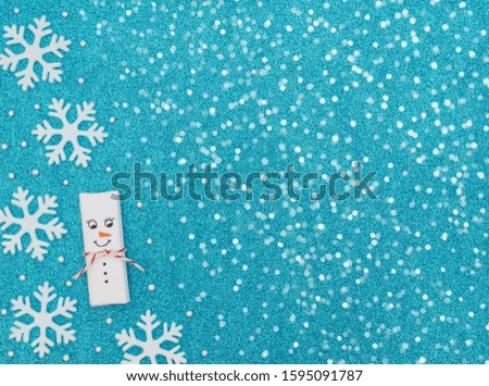 Christmas snowman with snowflakes and beads on blue background with white snow. New Year greeting card. Christmas, New Year concept. Flat lay style with copy space.