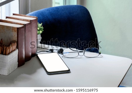 Workspace with smartphone, glasses, earphone, book and pencil on white table, home office workspace concept.