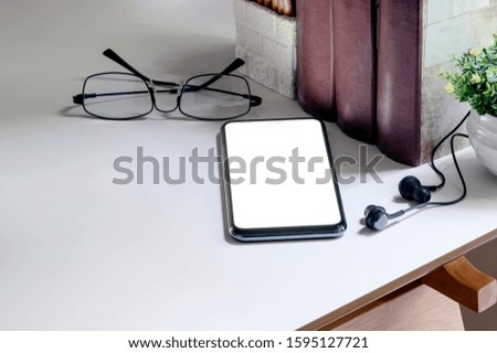 Workspace with smartphone, glasses, earphone, book and pencil on white table, home office workspace concept.