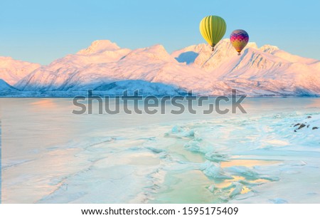 Beautiful winter landscape with Hot air balloon in the sky at amazing sunset - Cracking ice, frozen norwegian sea coast at sunrise - Tromso, Norway