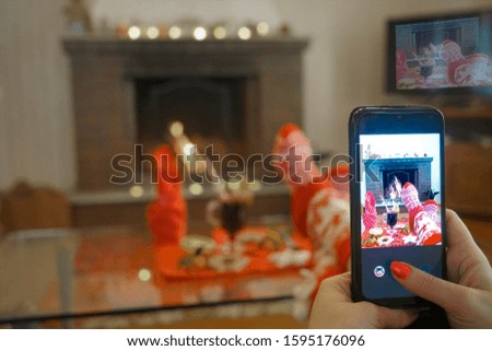 Hands taking picture of gingerbread cookies, red socks, gingerbread and fireplace. focus on screen. 