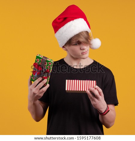 Young guy in a red santa hat holds a gift box in his hands and poses on a yellow background