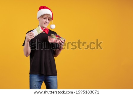Young guy in a red Santa Claus hat holds in his hands banknotes, money and posing on a yellow background