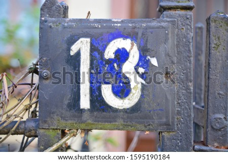 A blue colored house number plaque, showing the number thirteen (13)