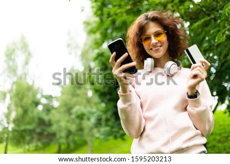 attractive girl with a phone and a credit card with a mockup on a background of green park