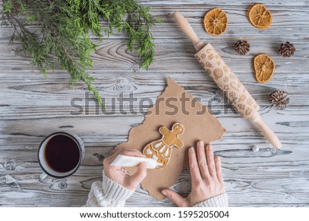 Woman decorating honey gingerbread men on wooden grey table and craft paper. Christmas Icing bakery. Flat lay
