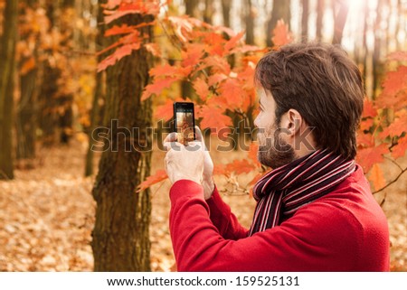 Forty years old caucasian man taking autumn outdoor photo with mobile phone - enjoying nature and modern technology