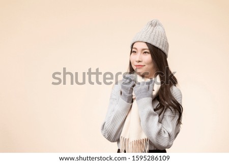 Portrait of young woman wearing winter clothes against beige background