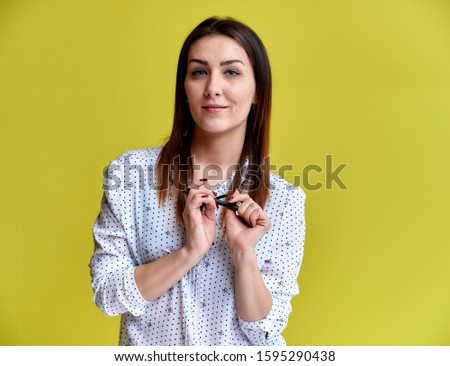 The concept of an office worker, teacher, manager. Portrait of a pretty brunette girl in a white business blouse smiling, talking to the camera on a yellow background.