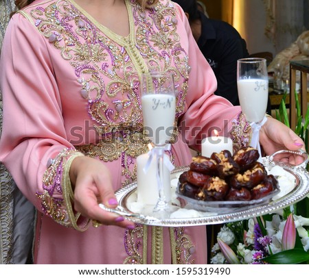 Moroccan woman in pink kaftan. She holds a cup of milk and dates in her hands, to present them to the newlyweds