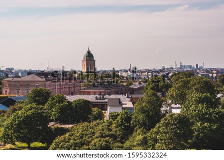 View of Suomenlinna and its old buildings and lighthouse with green trees on a summer day with the Helsinki in the background