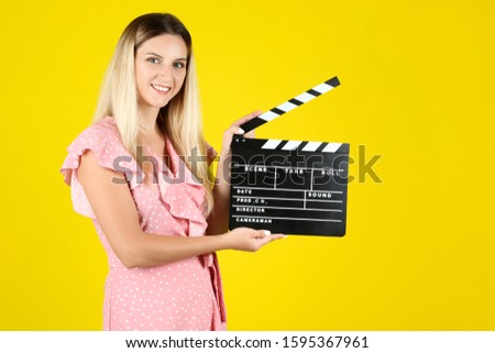 Young woman with blank clapper board on yellow background