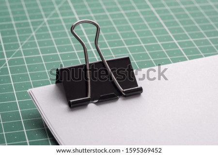 Big black paper clip on a pile of papers on a green cutting mat