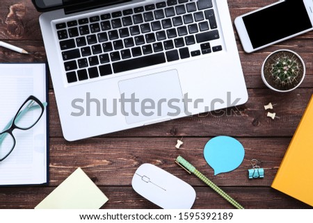 Laptop computer with office supplies and smartphone on brown wooden table