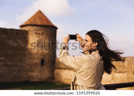 A happy young woman enjoying her trip to the castle while taking pictures and selfies. Brunette woman turn around. Girl enjoying her vacation. Tourist taking fun selfie.