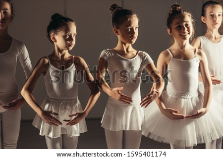 sweet little ballerinas in white tutu skirts stand in a row, group dance of classic ballet in studio, ballet school