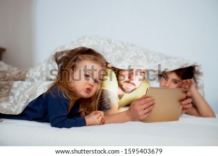 friendly emotional family, young parents and kids enjoy watching film lying on bed under blanket, leisure time