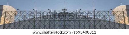 The large green steel billboard frame is located on the metal sheet roof in front of the factory under the blue sky and clouds