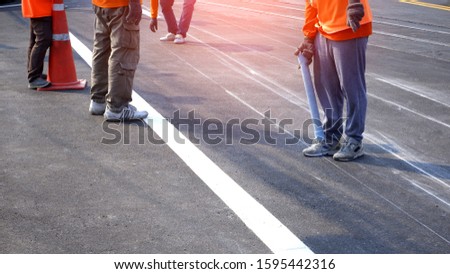 Cropped image of road workers group marking line for painting traffic color lines on asphalt road with railway track crossing on street surface 