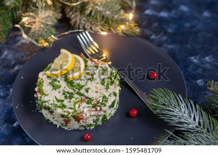 Tabbouleh salad in a dark plate on a blue background under concrete. Couscous, parsley with green onions and tomatoes and mint. Dressed with olive oil and lemon juice. Copy space.