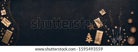 Golden Christmas decorations, gift boxes, champagne flutes on black background. Top view, copy space. Design element for greeting card, invitation, advertising. Extra wide panorama banner background