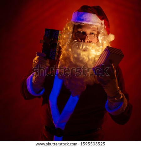 Santa Claus holds a gift box in his hands, looks into it and poses on a red background
