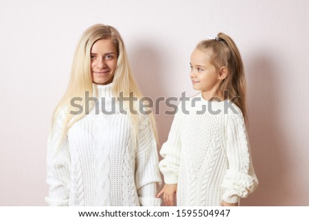 Love, family, care and relationships concept. Studio image of stylish young female with blonde long hair enjoying sweet moments of motherhood posing with her curious playful little daughter