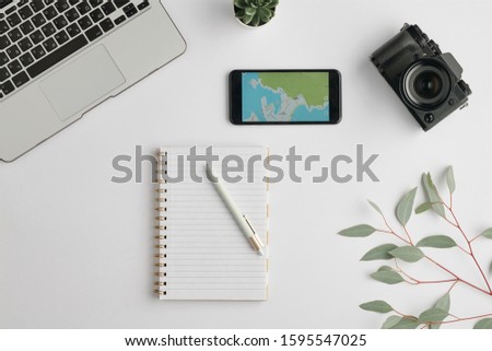 Flat layout of notebook with pen surrounded by smartphone, photocamera, laptop and branch with green leaves