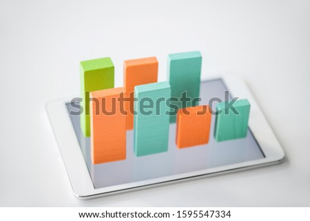 Two rows of flat wooden bricks making colorful chart on screen of digital tablet over white background