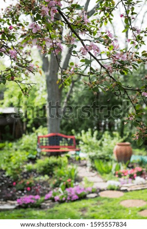 Beautiful flowers make up the foreground, with a cobblestone stone walkway leading to an old red antique bench, made of iron and wood, in the background