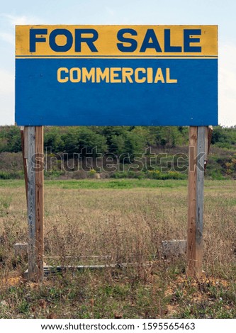 Blue and yellow FOR SALE COMMERCIAL sign in field.