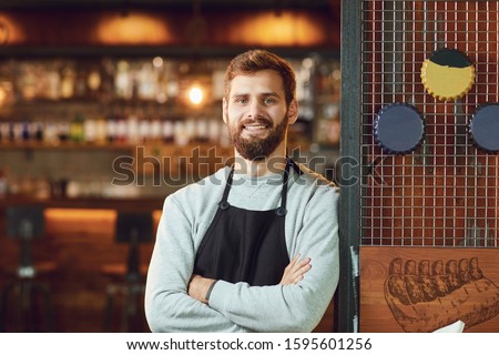 Bearded smiling barman waiter standing on the background of a bar. Royalty-Free Stock Photo #1595601256