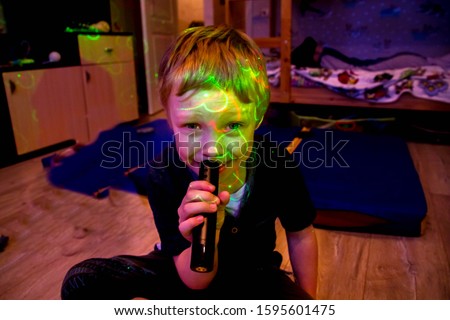 European boy 5 6 years old sings at home into the microphone. A child is a music lover loves to sing. Ear for music, karaoke. Laser light on the baby's face. Show, fun mood, party at home.
