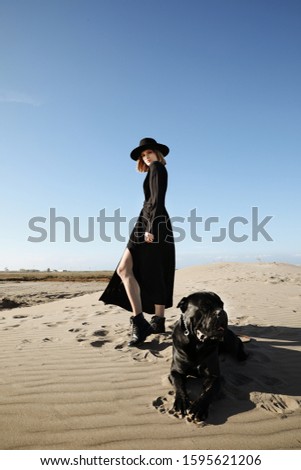 A woman standing on top of a sandy beach with dog.