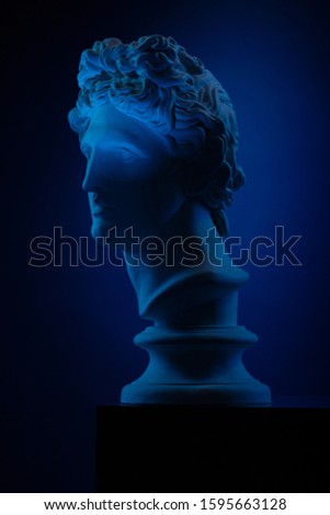 Statue of a bust of Apollo's head in blue local light on a blue background