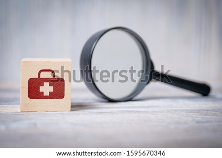 Close up of the cube with doctor's bag icon and magnifier on wooden background. Concept of search medical information, health.