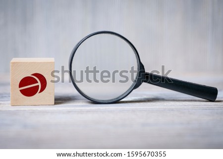 Close up of the cube with pills icon and magnifier on wooden background. Concept of search medical information, health.