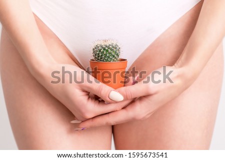 Woman holding a cactus in a pot on white panties background, epilation concept, intimate hygiene.