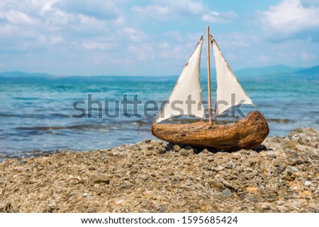 Miniature white and blue wooden boat with anchor lay on sand. Sailer Beach summer vacation background. Travel background. Seascape, cloudy sky on background. Sailer on the sea. Closeup