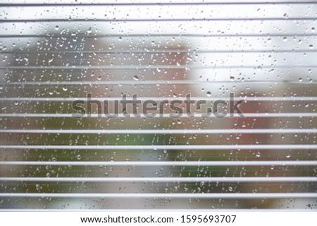 Rainy weather: wet window with raindrops, blinds and houses out of focus in background