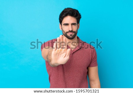 Young handsome man with beard over isolated blue background making stop gesture