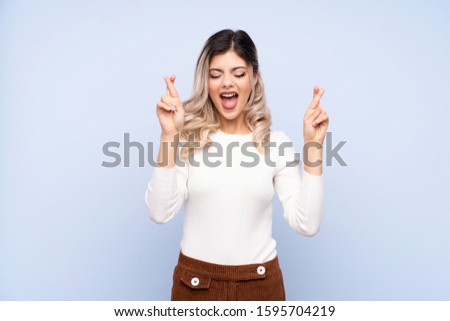 Young teenager girl over isolated blue background with fingers crossing