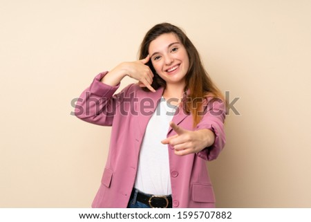 Young brunette girl with blazer over isolated background making phone gesture and pointing front