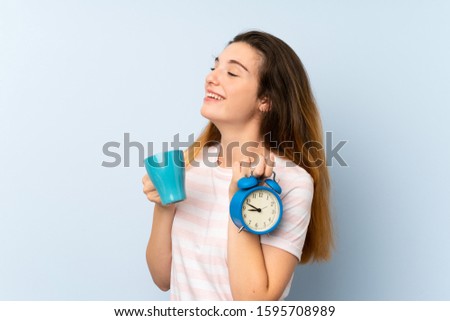 Young brunette girl holding a cup of coffee and vintage clock over isolated background