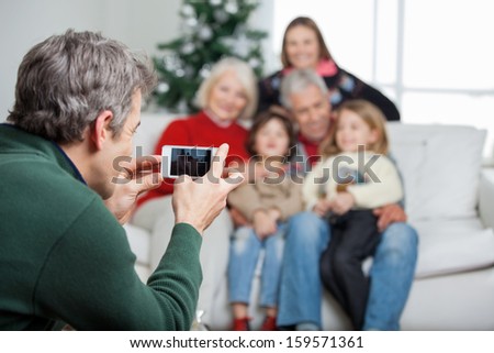 Father photographing family through smartphone at home