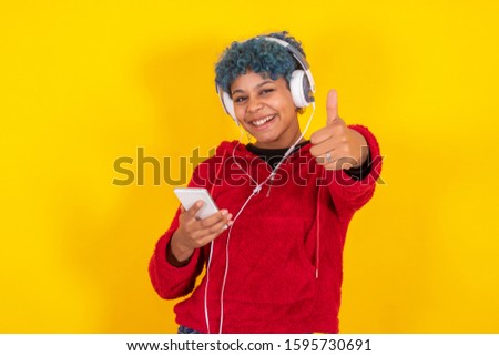 isolated young african american woman with mobile phone and headphones with expression of satisfaction and success
