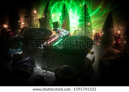 Christmas and New Year club concept. Dj mixer with headphones on snow. Santa Claus is mixing on turntable. Creative miniature artwork decoration on snow.
