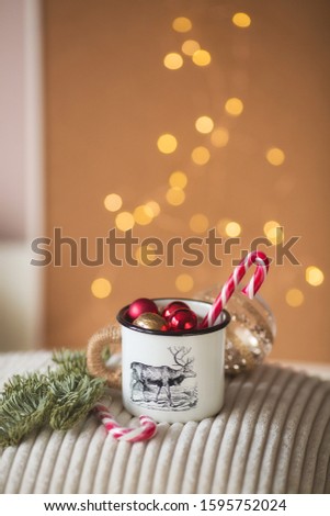 
mug with red balls on a knitted pillow on a background of beautiful golden bokeh. Cozy winter break. Warm, festive, atmospheric moment.